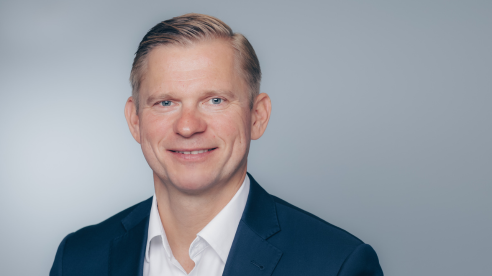 Smiling man in a navy suit and white shirt against a light gray background.